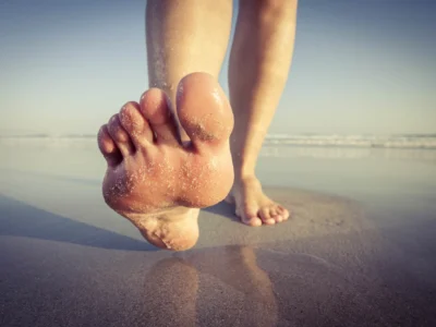 Big toe pain causes - person with big toe pain walking on a beach