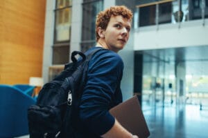 Young male student walking with a heavy bag