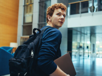 Young male student walking with a heavy bag